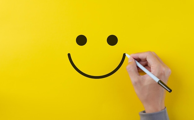 conceito de pesquisa de feedback de satisfação do cliente de revisão A mão usando caneta para desenhar um rosto sorridente feliz em fundo amarelo Negócio de avaliação de produtos de serviço Pensamento positivo Avaliação de saúde mental
