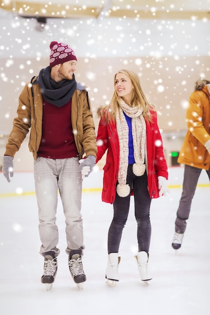 conceito de pessoas, amizade, esporte e lazer - casal feliz de mãos dadas na pista de patinação