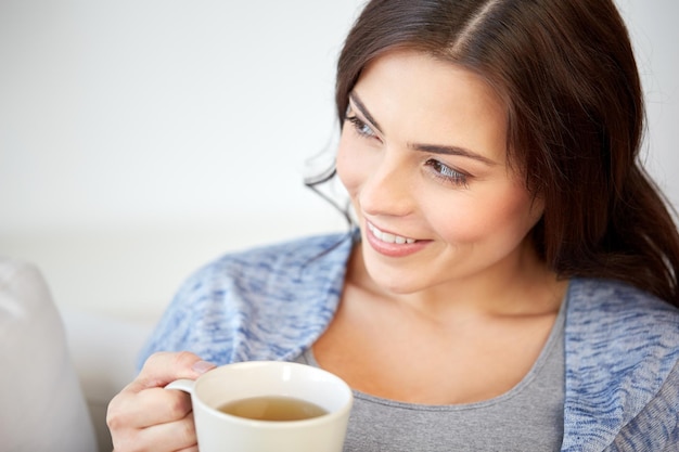 Conceito de pessoas, bebidas e lazer - jovem feliz com uma xícara de chá em casa