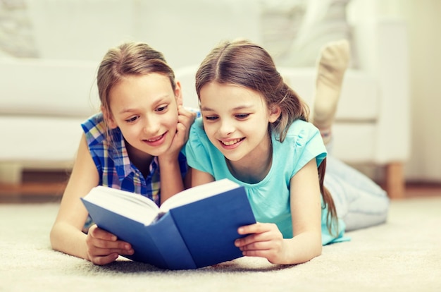 conceito de pessoas, crianças, amigos, literatura e amizade - duas meninas felizes deitadas no chão e lendo um livro em casa