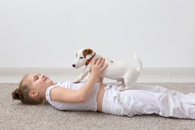 Conceito de pessoas, crianças e animais de estimação - menina criança deitada no chão com um cachorrinho fofo nas mãos.