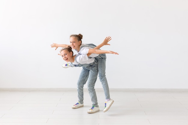 Conceito de pessoas, crianças e família - menina carregando sua irmã gêmea nas costas no fundo branco.