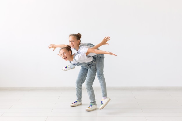 Conceito de pessoas, crianças e família - menina carregando sua irmã gêmea nas costas no fundo branco.