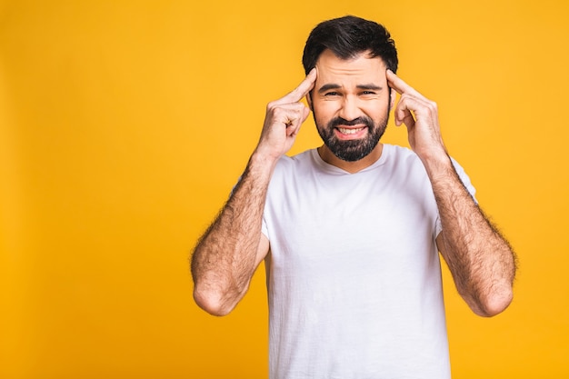 Foto conceito de pessoas, crise, emoções e estresse - homem cansado infeliz, sofrendo de dor de cabeça em casa. isolado sobre fundo amarelo.