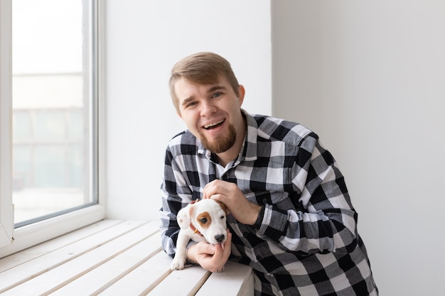 Conceito de pessoas e animais de estimação - homem feliz segurando um cachorro Jack Russell Terrier na janela