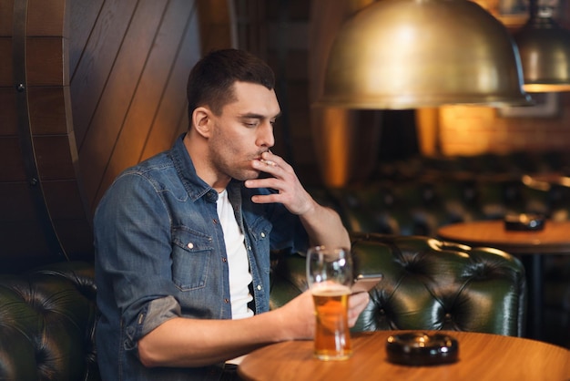 conceito de pessoas e maus hábitos - homem bebendo cerveja e fumando cigarro no bar ou pub