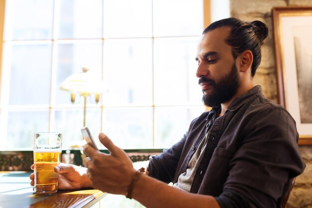 conceito de pessoas e tecnologia - homem com smartphone bebendo cerveja e lendo mensagem em bar ou pub