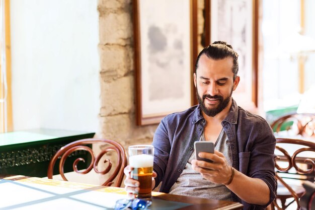 conceito de pessoas e tecnologia - homem com smartphone bebendo cerveja e lendo mensagem em bar ou pub