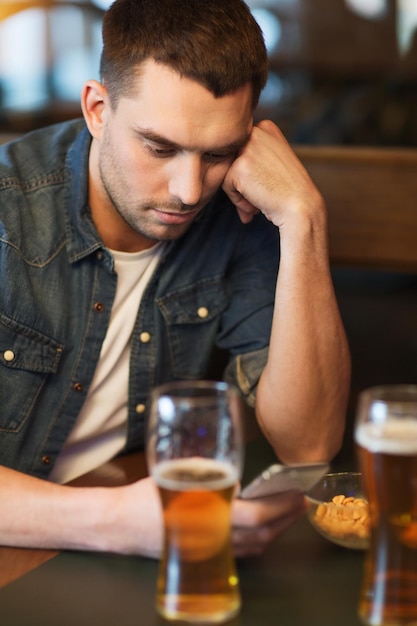 Conceito de pessoas e tecnologia - homem com smartphone bebendo cerveja e lendo mensagem no bar