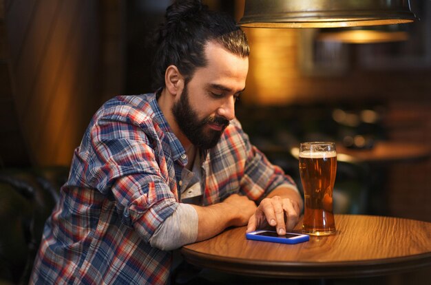 conceito de pessoas e tecnologia - homem feliz com smartphone bebendo cerveja e lendo mensagem no bar ou pub