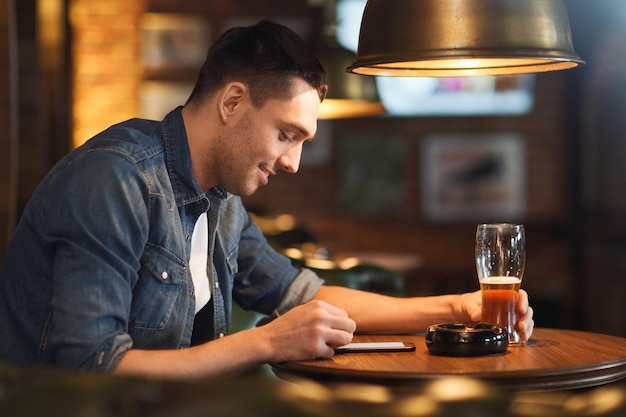 conceito de pessoas e tecnologia - homem feliz com smartphone bebendo cerveja e lendo mensagem no bar ou pub