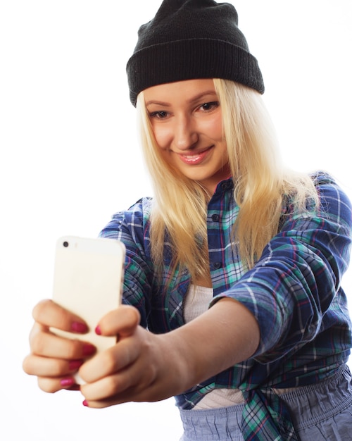 Conceito de pessoas, estilo de vida e tecnologia: muito adolescente usando chapéu, tirando selfies com seu telefone inteligente - isolado no branco