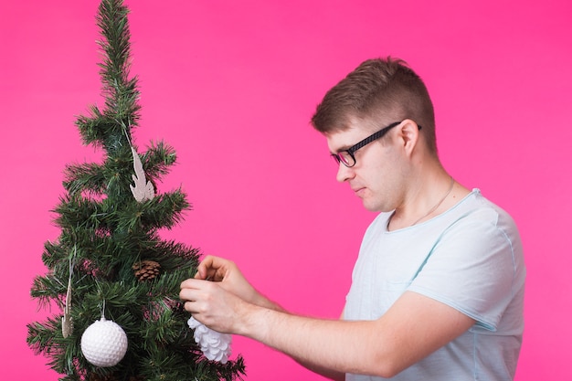Conceito de pessoas, feriados e natal - jovem decorando uma árvore de natal em fundo rosa