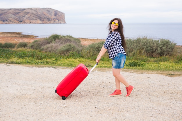 Conceito de pessoas, férias e viagens - bela jovem em pé com a mala na superfície do mar.