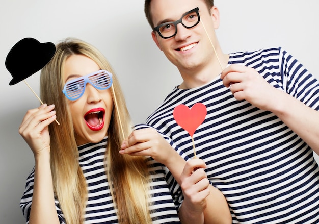 Conceito de pessoas, festa, amor e lazer - lindo casal segurando óculos de festa e chapéu em palitos, sobre fundo cinza