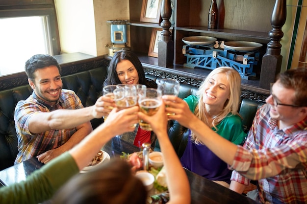 conceito de pessoas, lazer, amizade e celebração - amigos felizes bebendo chope e tilintar de copos em bar ou pub