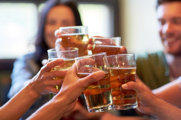 conceito de pessoas, lazer, amizade e celebração - amigos felizes bebendo chope e tilintar de copos em bar ou pub