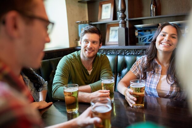 conceito de pessoas, lazer, amizade e comunicação - amigos felizes bebendo cerveja e conversando no bar ou pub