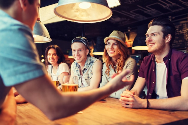 conceito de pessoas, lazer, amizade e comunicação - grupo de amigos sorridentes felizes bebendo cerveja e conversando no bar ou pub