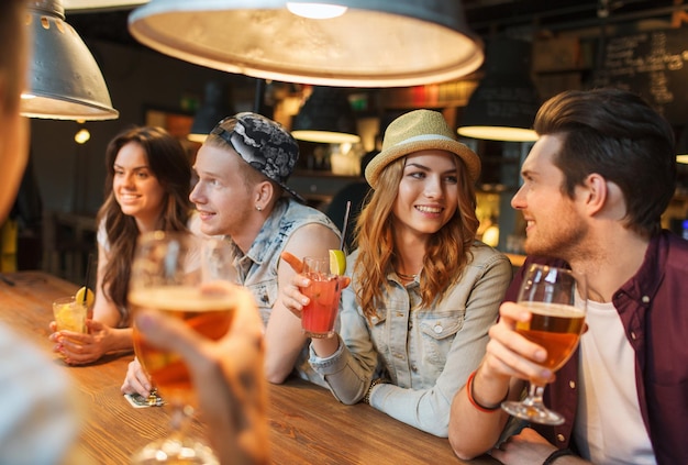 conceito de pessoas, lazer, amizade e comunicação - grupo de amigos sorridentes felizes bebendo cerveja e coquetéis conversando no bar ou pub