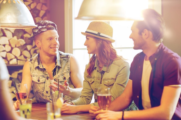 conceito de pessoas, lazer, amizade e comunicação - grupo de amigos sorridentes felizes bebendo cerveja e coquetéis no bar ou pub