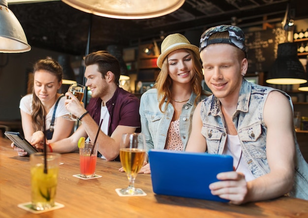 conceito de pessoas, lazer, amizade e comunicação - grupo de amigos sorridentes felizes com computador tablet pc e bebidas no bar ou pub