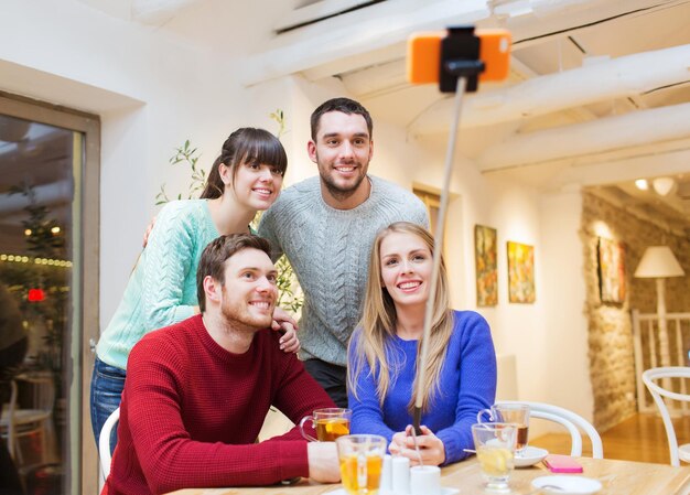 conceito de pessoas, lazer, amizade e tecnologia - grupo de amigos felizes com smartphone selfie stick tirando foto e bebendo chá no café