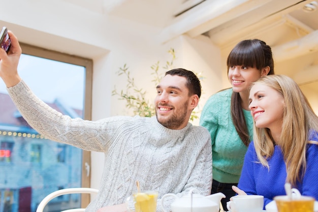 conceito de pessoas, lazer, amizade e tecnologia - grupo de amigos felizes com smartphone tomando selfie e bebendo chá no café