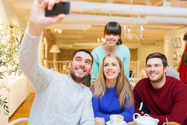 conceito de pessoas, lazer, amizade e tecnologia - grupo de amigos felizes com smartphone tomando selfie e bebendo chá no café