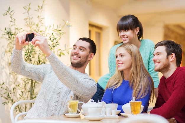 conceito de pessoas, lazer, amizade e tecnologia - grupo de amigos felizes com smartphone tomando selfie e bebendo chá no café