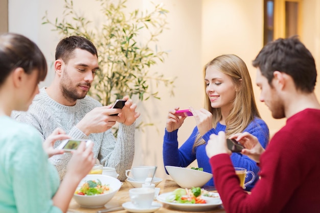 conceito de pessoas, lazer, amizade e tecnologia - grupo de amigos felizes com smartphones tirando foto de comida no café