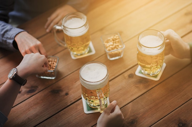 conceito de pessoas, lazer e bebidas - close-up de mãos masculinas com canecas de cerveja e amendoim no bar ou pub