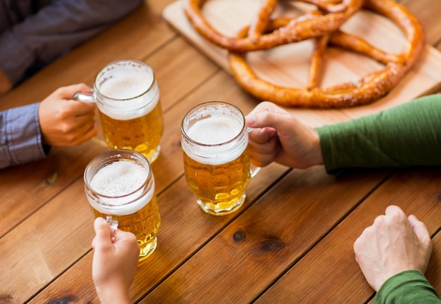 conceito de pessoas, lazer e bebidas - close-up de mãos masculinas com canecas de cerveja e pretzels no bar ou pub