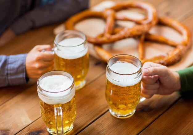 conceito de pessoas, lazer e bebidas - close-up de mãos masculinas com canecas de cerveja e pretzels no bar ou pub