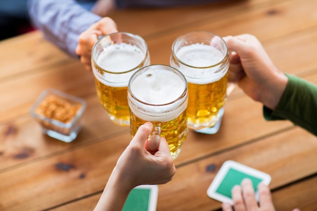 conceito de pessoas, lazer e bebidas - close-up de mãos tilintando canecas de cerveja no bar ou pub