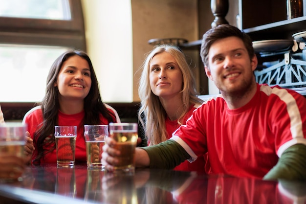 conceito de pessoas, lazer e esporte - amigos felizes ou fãs de futebol bebendo cerveja e assistindo jogo de futebol ou partida em bar ou pub