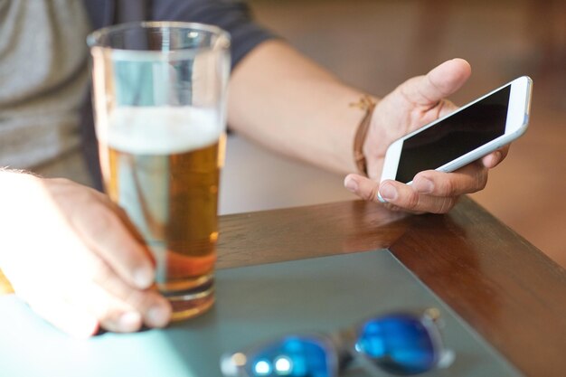 conceito de pessoas, lazer e tecnologia - close-up do homem com smartphone bebendo cerveja e lendo a mensagem no bar ou pub