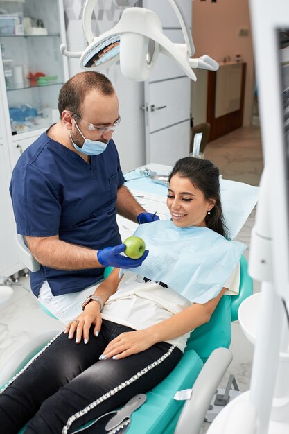 Foto conceito de pessoas, medicina, estomatologia e cuidados de saúde - dentista masculino feliz, mostrando o plano de trabalho para uma paciente no consultório da clínica odontológica.