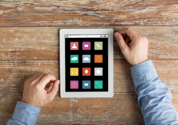 Foto conceito de pessoas, multimídia e tecnologia - close-up de mãos masculinas com ícones de menu na tela do computador tablet pc na mesa de madeira