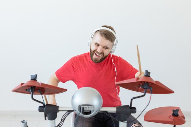 Conceito de pessoas, música e passatempo - Homem com fones de ouvido brancos tocando bateria sobre a luz