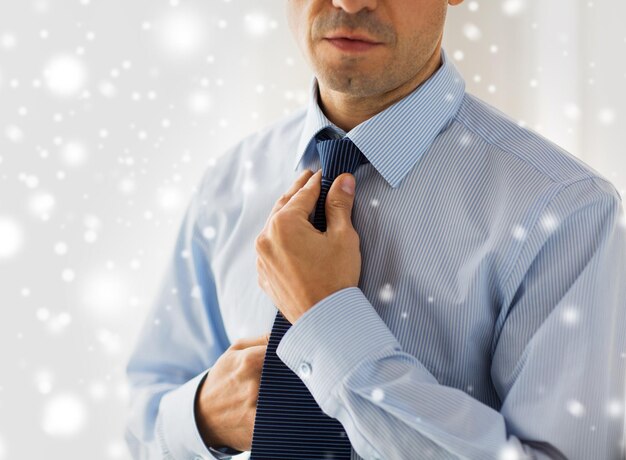 Conceito de pessoas, negócios, moda e roupas - close-up do homem de camisa vestindo-se e ajustando a gravata no pescoço em casa sobre o efeito de neve