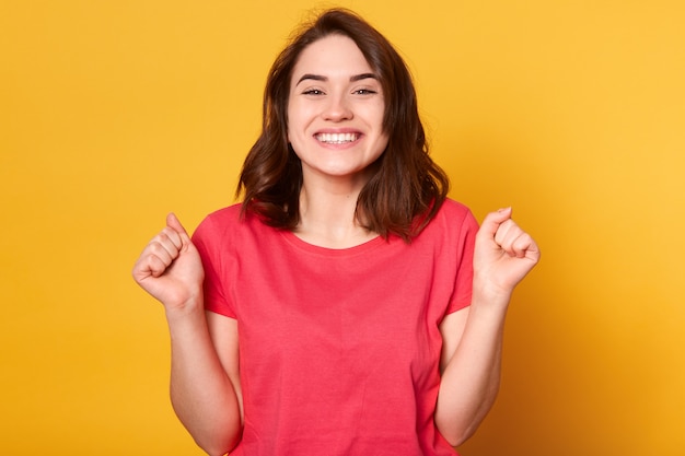 Conceito de pessoas, sucesso, vitória, vitória e conquista. Alegre mulher morena sortuda animada, cerrando os punhos e sucesso selebrating