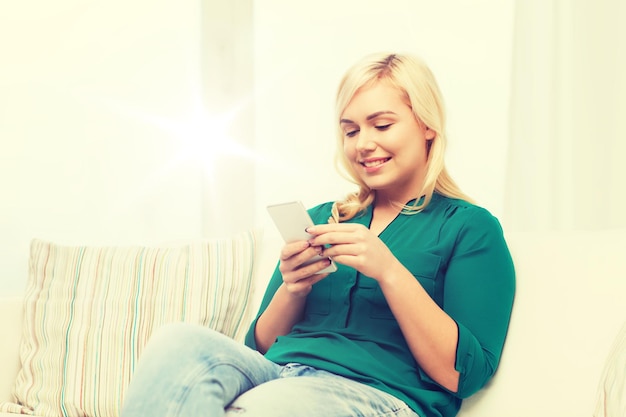 conceito de pessoas, tecnologia, comunicação e lazer - jovem feliz sentada no sofá com smartphone em casa