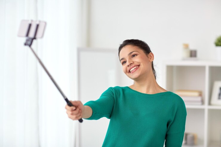 Foto conceito de pessoas, tecnologia e estilo de vida - mulher feliz tirando fotos com bastão de selfie de smartphone ou monopé em casa
