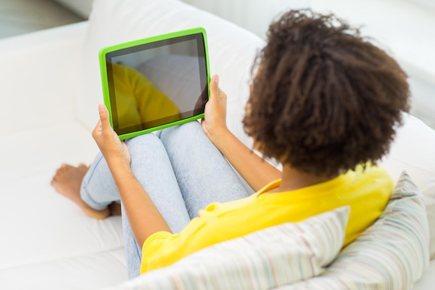 conceito de pessoas, tecnologia, propaganda e lazer - jovem afro-americana feliz sentada no sofá com tela em branco preta do computador tablet pc em casa