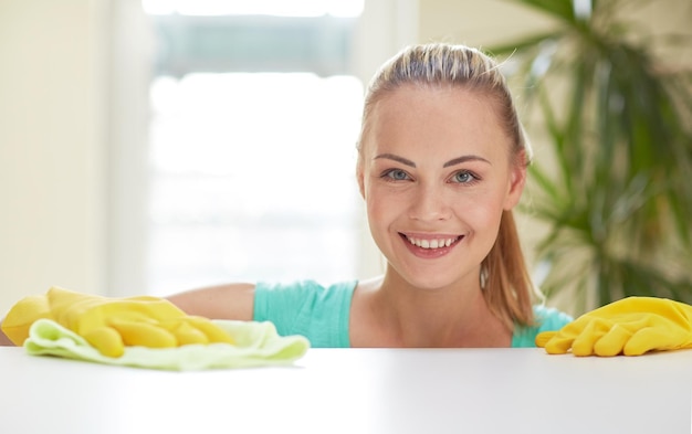 Conceito de pessoas, trabalho doméstico e limpeza - mulher feliz limpando a mesa na cozinha de casa