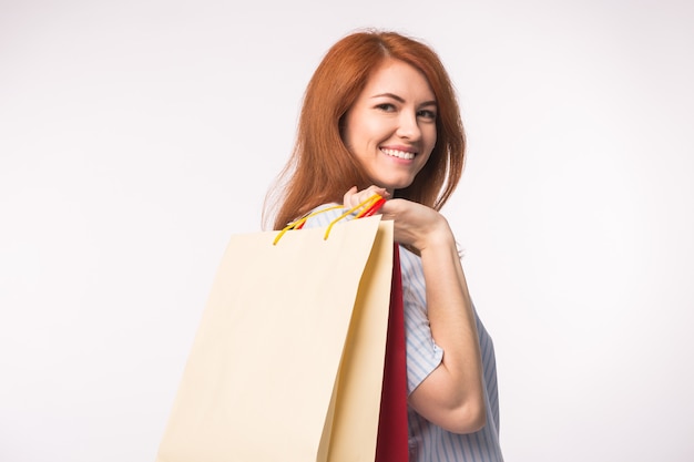 Conceito de pessoas, venda e consumismo - mulher atraente com cabelo vermelho sobre uma superfície branca, segurando sacolas de compras.