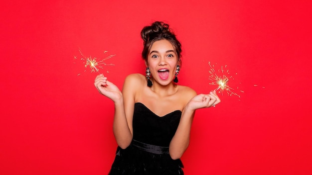 Conceito de pirotecnia e pessoas sorrindo jovem ou adolescente mulher feliz com estrelinhas celebram em vestido preto em fundo vermelho menina feliz com a boca aberta