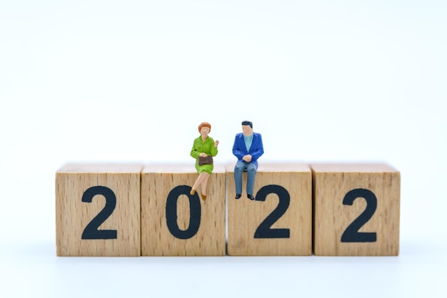 Conceito de planejamento de ano novo de 2020 Closeup da figura em miniatura de empresário e empresária sentado e falando na pilha de bloco de números de madeira isolado no fundo branco