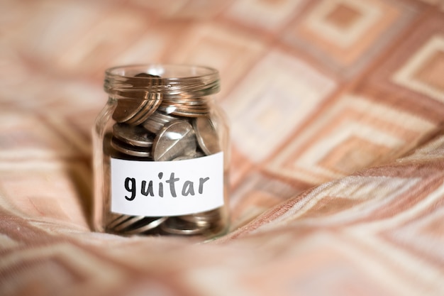 Conceito de poupança para guitarra - frasco de vidro com moedas e inscrição.